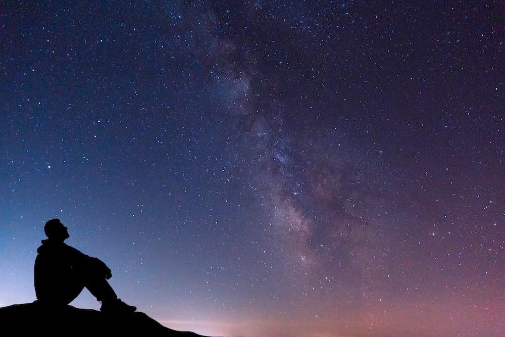 silhouette of man sitting under a starry sky